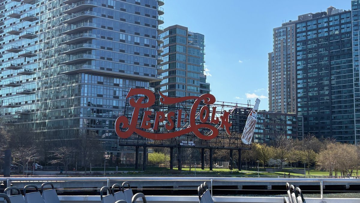 Iconic Pepsi-Cola sign in Long Island City, Queens, with modern NYC skyscrapers.
