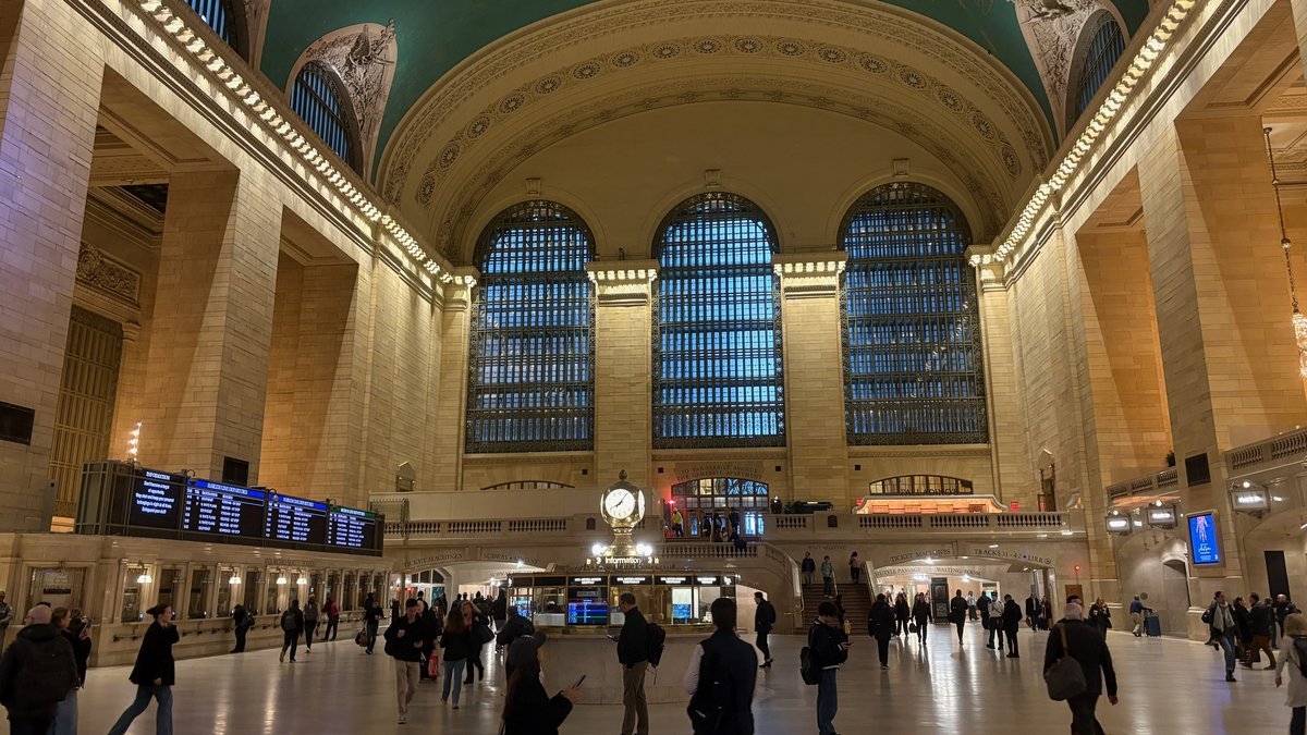 Grand Central Terminal main concourse with iconic clock and arched windows, bustling with people.