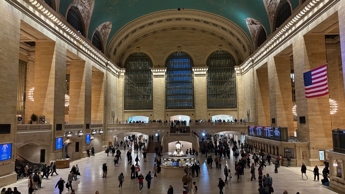 Interior majestuoso de Grand Central Terminal en Nueva York con gente y bandera.