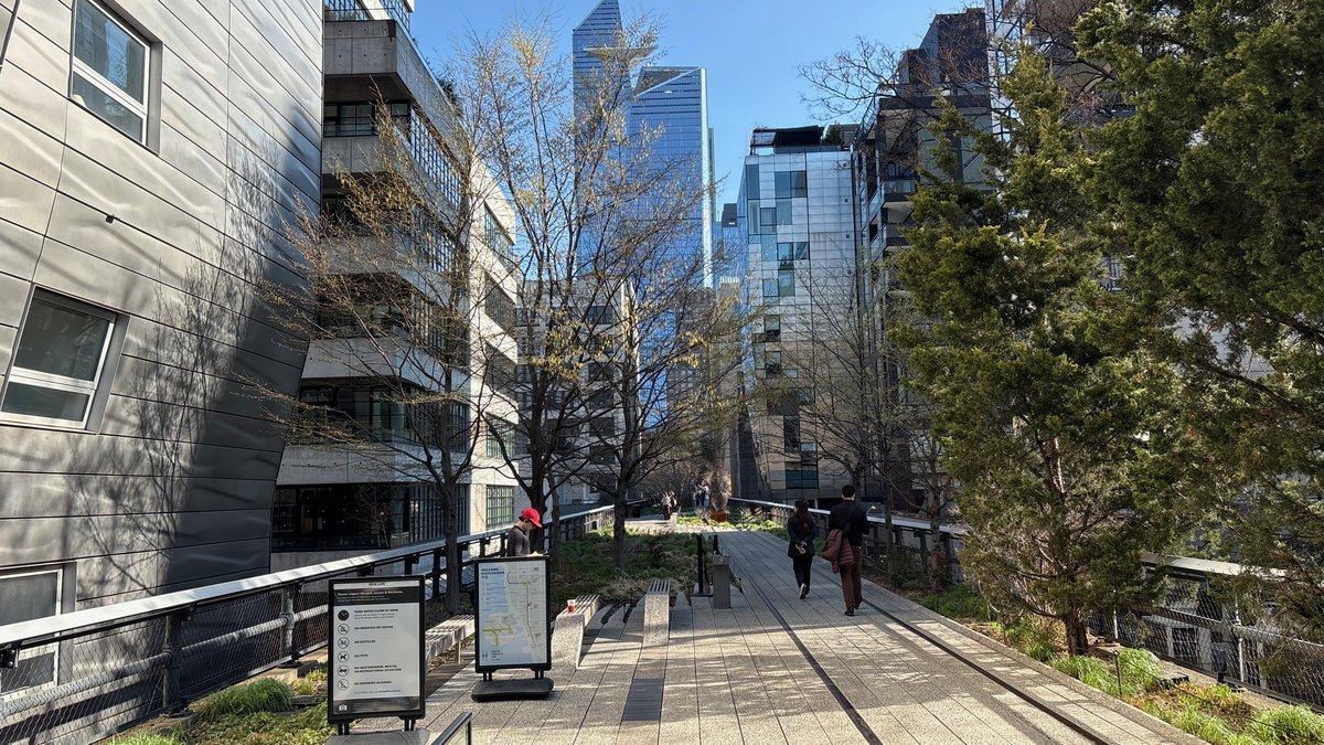 The High Line urban park in NYC on a sunny day with modern architecture and pedestrians.