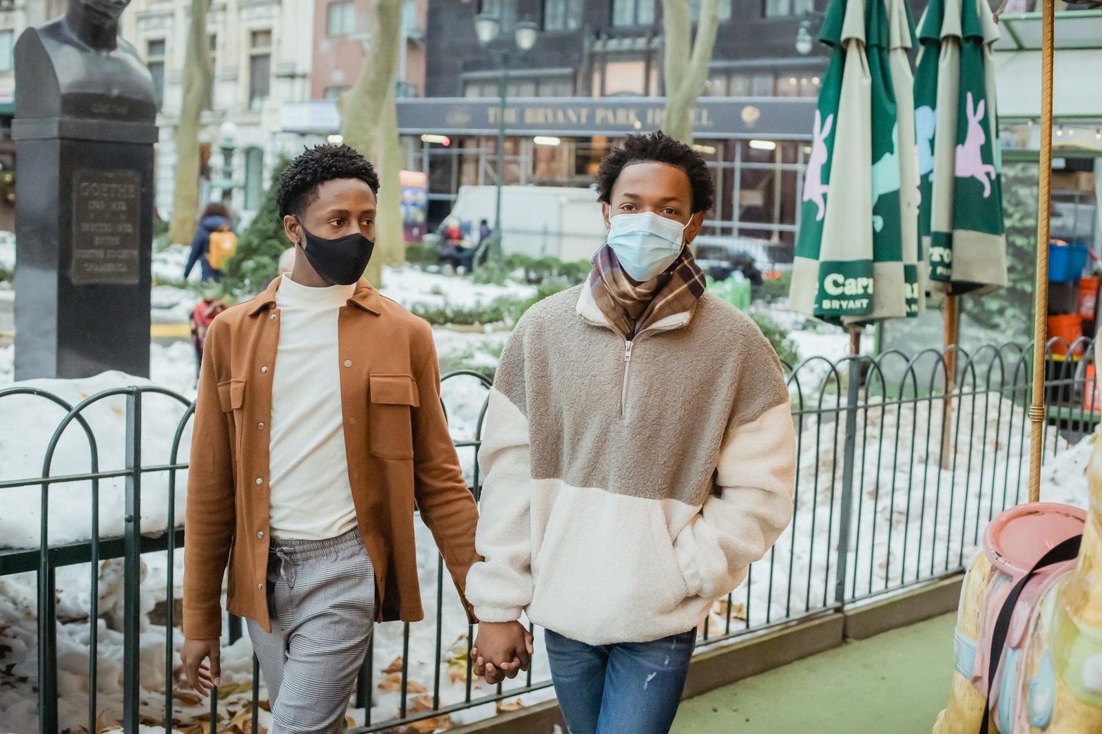 Two masked men holding hands in snowy Bryant Park, Midtown Manhattan.