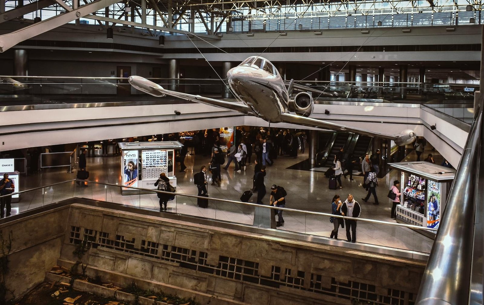 LaGuardia Airport Terminal B interior with suspended jet, travelers, and shops.