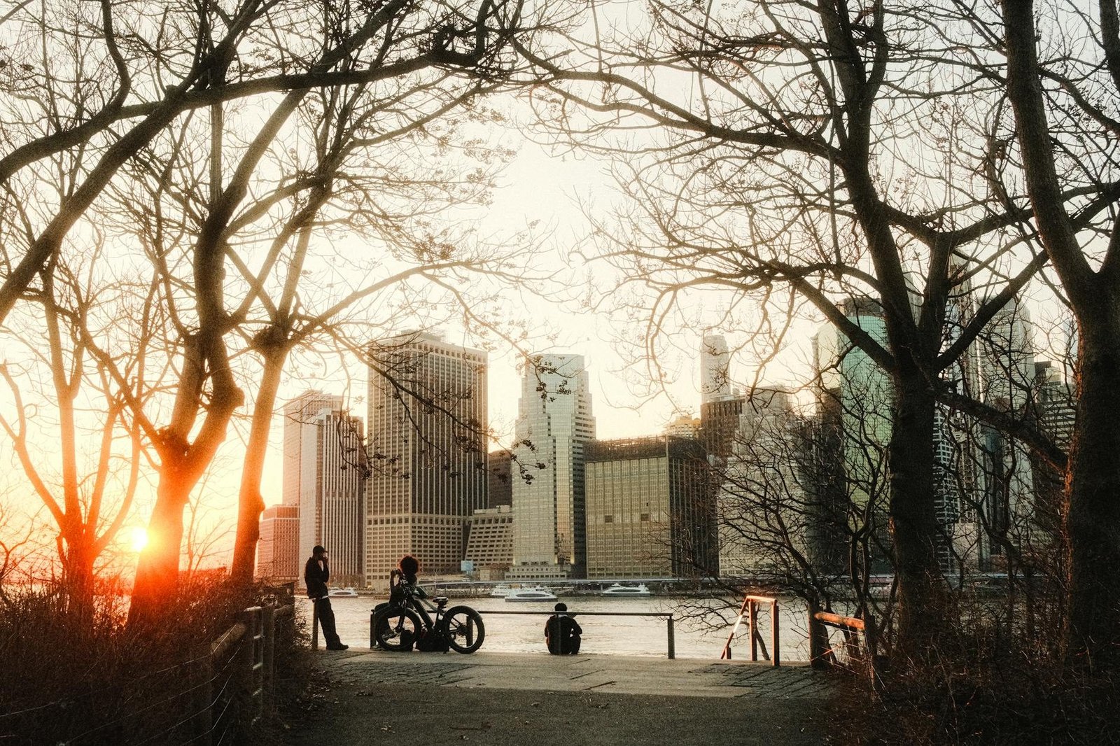 Sunset view of Lower Manhattan skyline from Brooklyn Bridge Park with people and bikes.