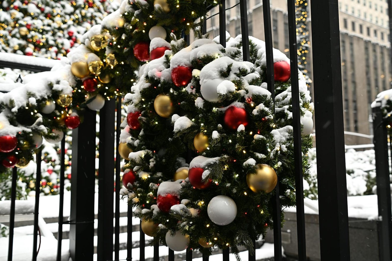 Snowy Christmas wreaths with red and gold ornaments on a fence in New York City.