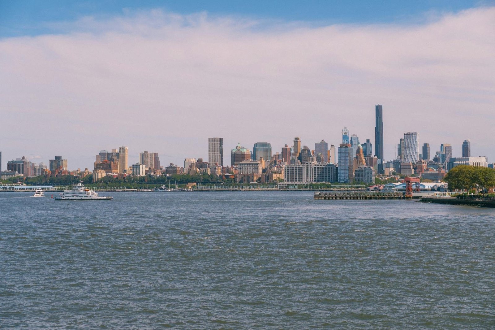 Panoramic view of New York City skyline from across the Hudson River with a ferry.