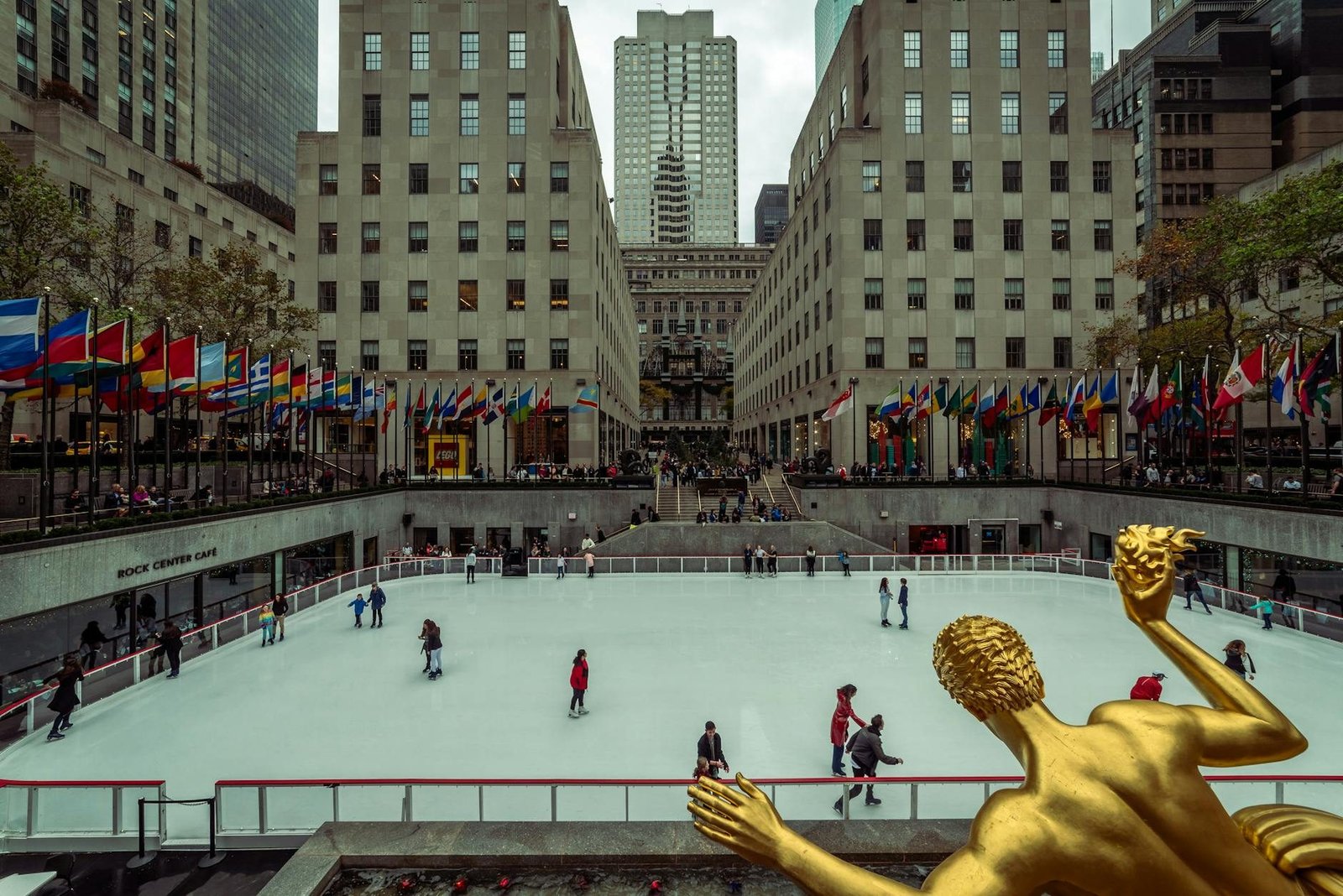 Rockefeller Center ice rink with skaters, flags, and Prometheus statue in New York City.