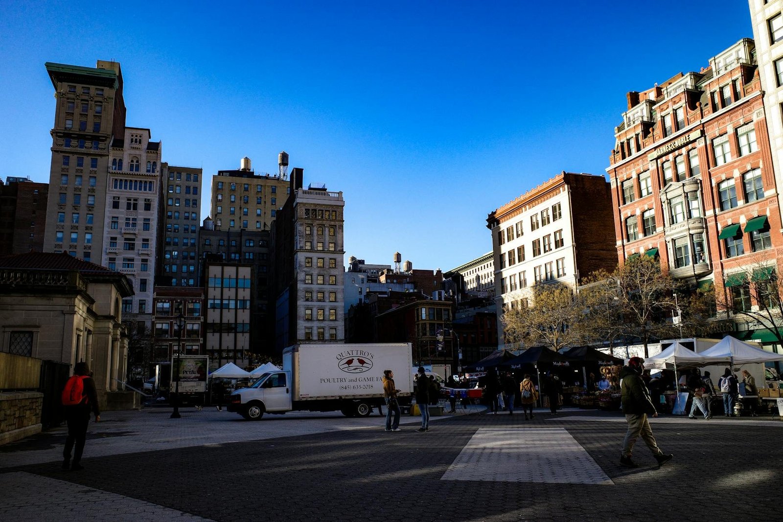 Union Square Park farmers market scene with historic NYC buildings and people.